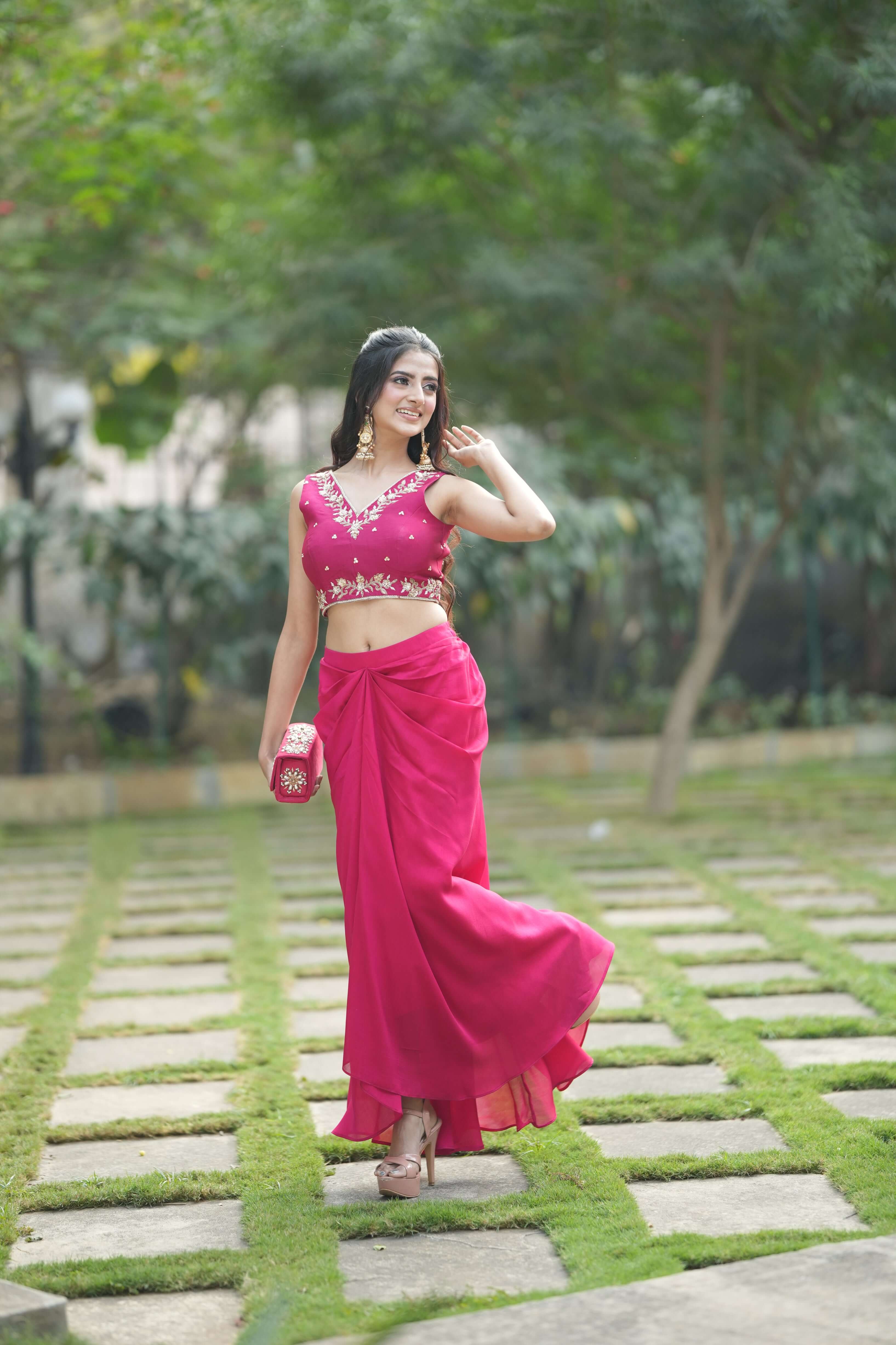 Stylish woman in pink embroidered crop top and flowy dhoti skirt, walking gracefully outdoors.